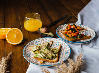 Spinach and avocado toasts with red bell pepper, fresh squeezed orange juice on dark wooden board. Healthy Breakfast concept.