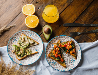 Avocado and spinach toasts with red bell pepper, fresh squeezed orange juice on dark wooden board. Vegetarian food, healthy diet concept.