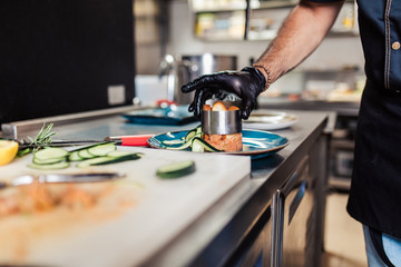 Professional chef in restaurant kitchen preparing delicious meal with meat and vegetables.