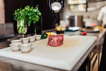 Professional chef in restaurant kitchen preparing delicious meal with meat and vegetables.