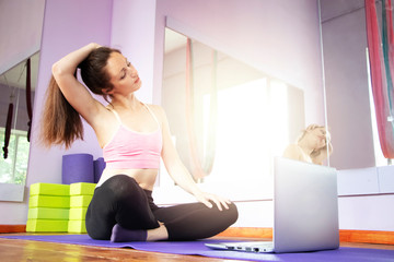 Fitness and yoga trainer teaches via laptop. Wireless technology in sports, self-isolation . The girl shows exercises in the gym on the mat. The concept of distance learning.