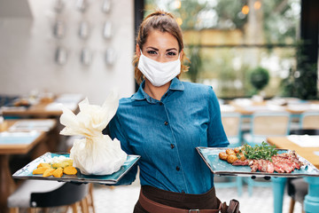 Beautiful young waitress with face protective mask working in exclusive restaurant. Coronavirus or...