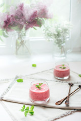 Two glasses of homemade berry smoothie decorated with mint leaves over white napkins in the kitchen. Healthy lifestyle.