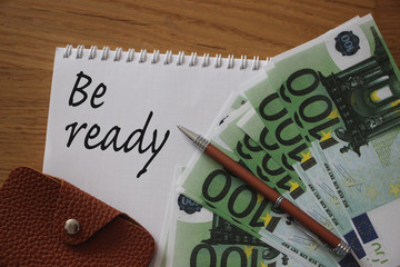 100 euro money, wallet, pen and copybook with Be Ready words. on wooden table, top view. Business...