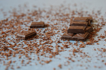 Macro photo of Broken pieces Chocolate bar. Dark chocolate stack with brown powder on a stone background with copy space.