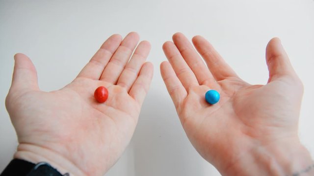 Male hands appear in frame hold and reveal two opposite colourful pills. Blue and red candy or meds to choose from. Concept decision making or indecisiveness 