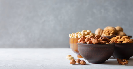 Nuts in wooden and clay bowls on a gray background with a copy space. Hazelnuts, cashews, almonds and walnuts. Banner.