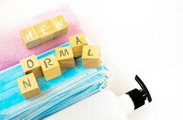 Top view wooden cubes texts on face masks and towel over white. Hand sanitizer in visibility. Conceptual embracing new normal as lifestyle due to Covid-19. Selective focus on wooden cubes only.