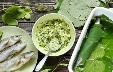 the process of making small fish in grape leaves. the fish is stuffed with couscous with herbs and wrapped in a grape leaf, watered with oil and baked in the oven.