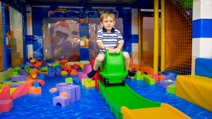 Happy little boy riding on plastic toy ca on the playground at shopping mall