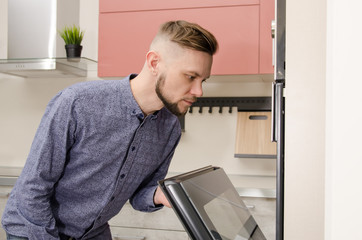 attractive bearded man peeks into an oven in a modern kitchen