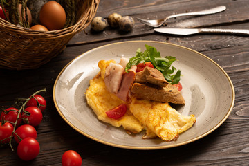 Omelet with bacon, cherry tomatoes, arugula and bread is beautifully served on a dark wooden table. Healthy breakfast of eggs and vegetables.