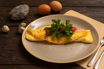 Omelet with bacon, cherry tomatoes and arugula are beautifully served on a dark wooden table. Healthy breakfast made from eggs of salad and vegetables.