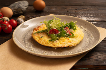 Omelet with cheese, cherry tomatoes and arugula are beautifully served on a dark wooden table. Healthy breakfast made from eggs of salad and vegetables.