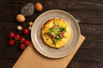Omelet with cheese, cherry tomatoes and arugula are beautifully served on a dark wooden table. Healthy breakfast made from eggs of salad and vegetables, top view.