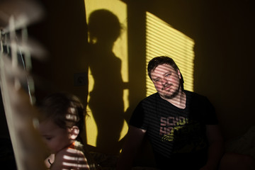 
dad with children plays at home on a sunny day. family in the shade of the blinds. Dad and children having fun in the bedroom on a sunny day. The shadow of the blinds in the room with the family