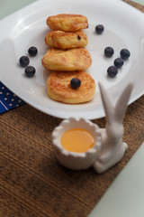 Syrniki or cottage cheese pancakes with blueberries and honey on white plate with blue napkin on kitchen table. Healthy breakfast, diet concept.