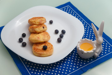 Syrniki or cottage cheese pancakes with blueberries and honey on white plate with blue napkin on kitchen table. Healthy breakfast, diet concept.