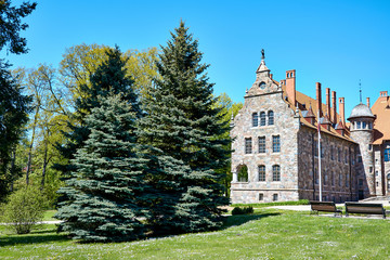 Cesvaine, Latvia - Cesvaine castle - a manor house of the late 19th century, a building of stones of different colors with a brown tiled roof, beautiful spruce trees, green grass, benches nearby.