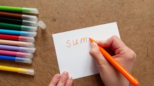 The girl writes on paper a marker word summer and sun.
