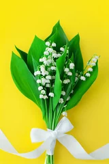 Keuken spatwand met foto Lily of the valley flower bouquet & white bowknot on yellow background closeup, beautiful may lilies bunch & green leaves with ribbon, convallaria majalis, romantic greeting card, bright floral design © Vera NewSib