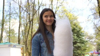 excited girl with long hair holds large cotton candy and walks along amusement park road slow motion close view