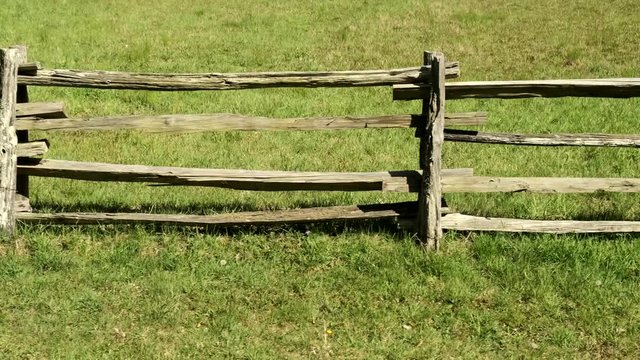 Rural split wooden rail fence along countryside green grass and landscape, sideways close up view