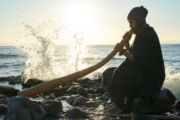 Silhouette of man playing didjireedoo in sunshine at seashore