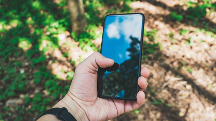 Young traveler hiking man walking through the woods with a mobile phone in his hand .