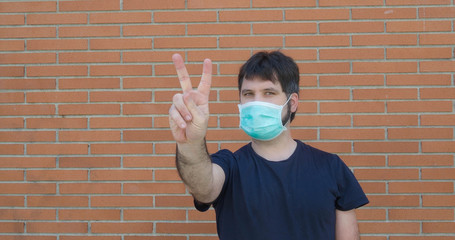 Man with mask makes with his fingers the symbol of victory on the street. Coronavirus security measures	