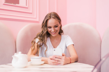 Young gorgeous lady chatting on her smart phone while relaxing in cafe after walking during summer weekend