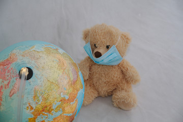 A teddy bear in a medical mask looks at the globe