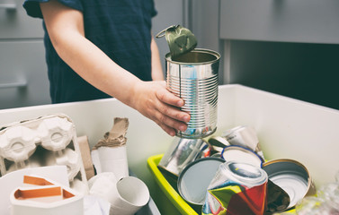 The boy is throwing the metal garbage to the one of four different bin for sorting trash.