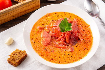 soup, Russian borscht with sour cream and parsley in a white plate, garlic, spoon, bread, on a white towel on a brown wooden background top view