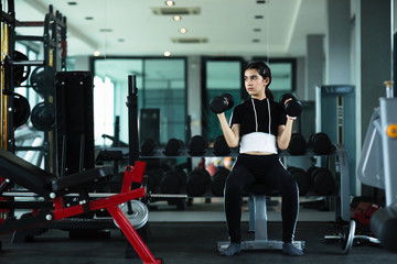 Young beautiful girl doing exercises with dumbbell in gym.