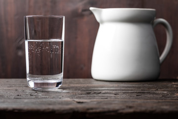 A glass of water with traces of limestone is placed on a rustic wooden board, a jar of white water in the background and the textured wood, as well as the natural light gives the scene a rural look.