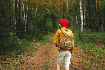 Tourist with a backpack is walking in the dark forest among the trees. Active trekking and unity with nature