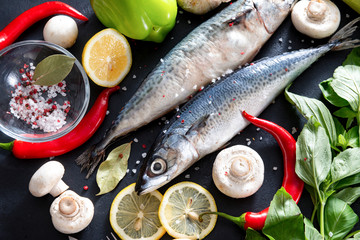 2 raw mackerel fish with chili , lemon slices, Basil,  mushrooms, salt  and spices on a black background,