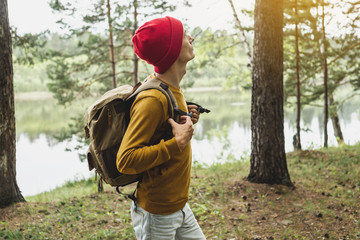 Naklejka premium Tourist with a backpack and a red hat is walking in the forest among the trees. Active trekking and unity with nature