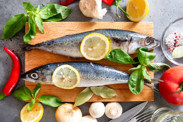 fish with spices and lemon slices, chili peppers, mushrooms, oil, tomato, Basil, garlic, onion, on the kitchen Board on a gray