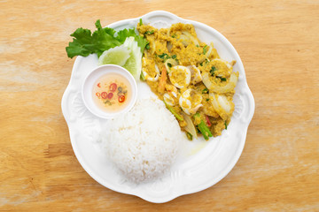 Stir fried squid in curry powder with rice and fish sauce mixed chili in white dish on wooden table.