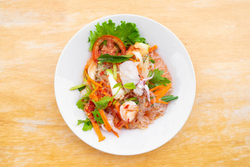 spicy vermicelli salad with seafood in white dish on wooden table.