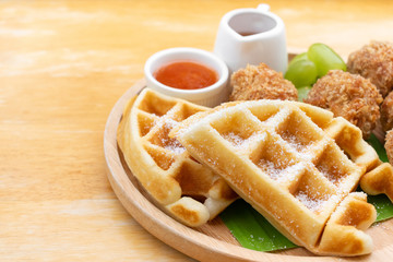 Waffles with fried chicken ball and grape in wooden dish on wooden table.