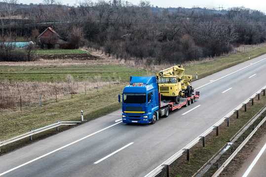 Transportation Tow truck or Flatbed truck on a highway carrying a construction machine to a site under a beautiful sky on a highway. Tow transportation concept