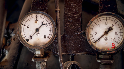 Closeup image of two rusty manometers with analog dials connected to vintage pipes of steam engine