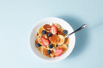 Mini pancake cereal with berries and honey on blue background	