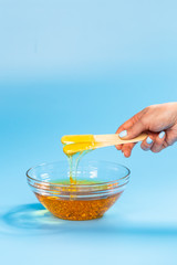 Liquid yellow wax or sugar paste for depilation drains from the stick on blue background. The concept of depilation, waxing, sugaring smooth skin without hair.