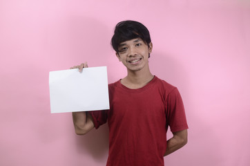 The young man holds a blank poster for writing and text. Asian men wearing red t shirts isolated on a pink background