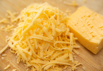 Cheese grated on a grater lies in a pile on the Board. There's a whole piece of cheese next to it. Yellow cheese.