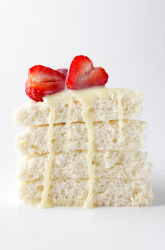 Verticl image.Piece of biscuit cake with slices of strawberry and condensed milk on the white background